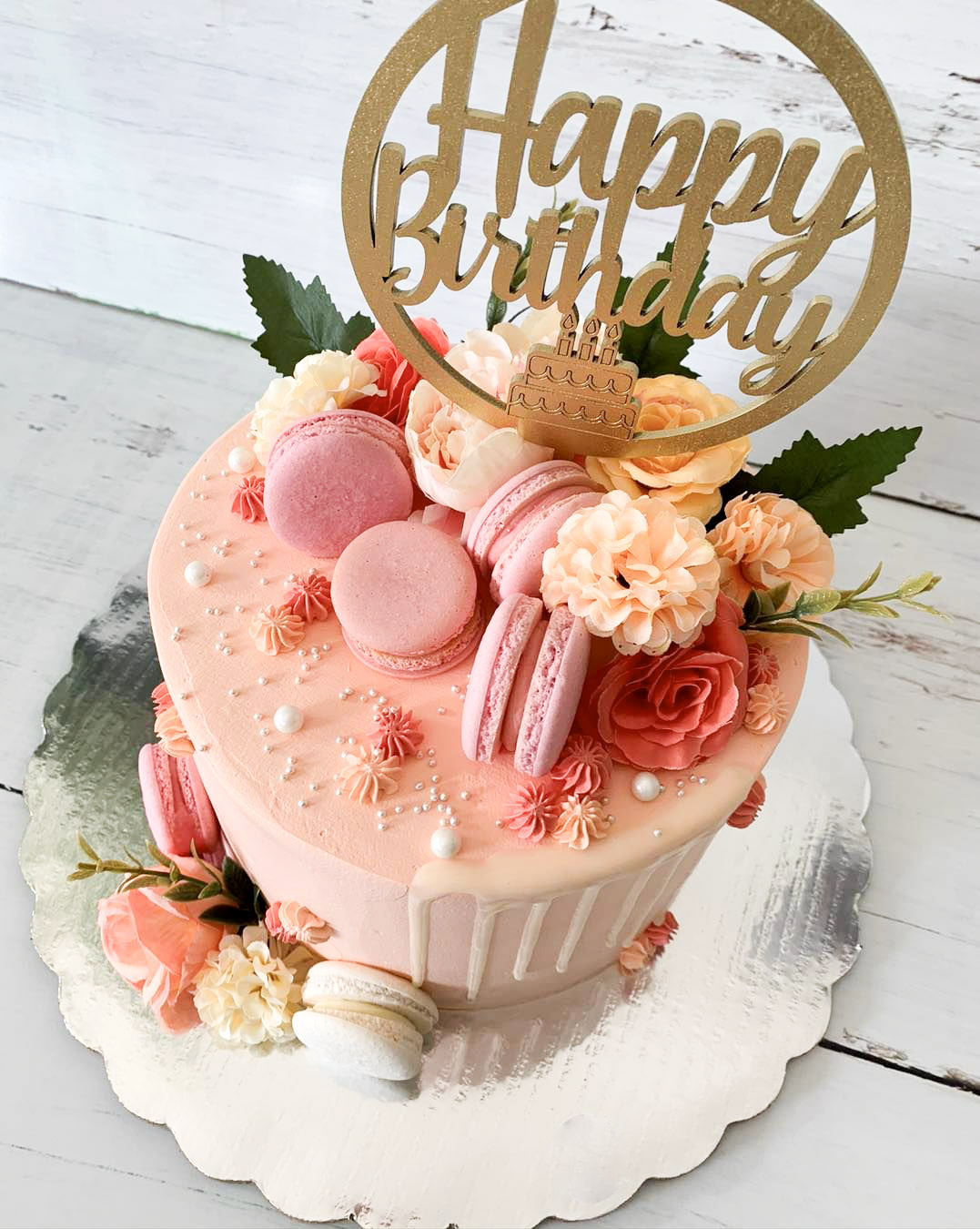 Pastel de cumpleaños con macarrns y flores en colores rosa y coral